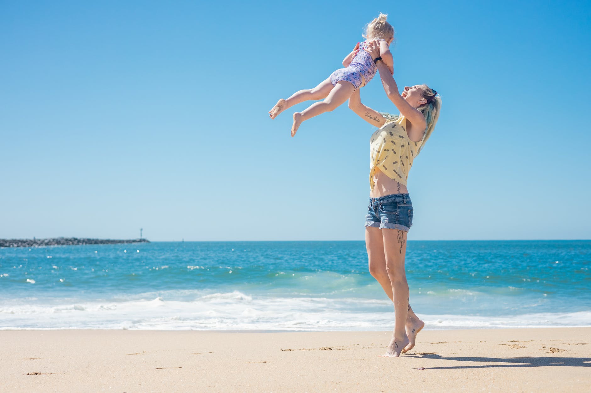 a woman throwing her daughter in the air while standing on the beach sand
